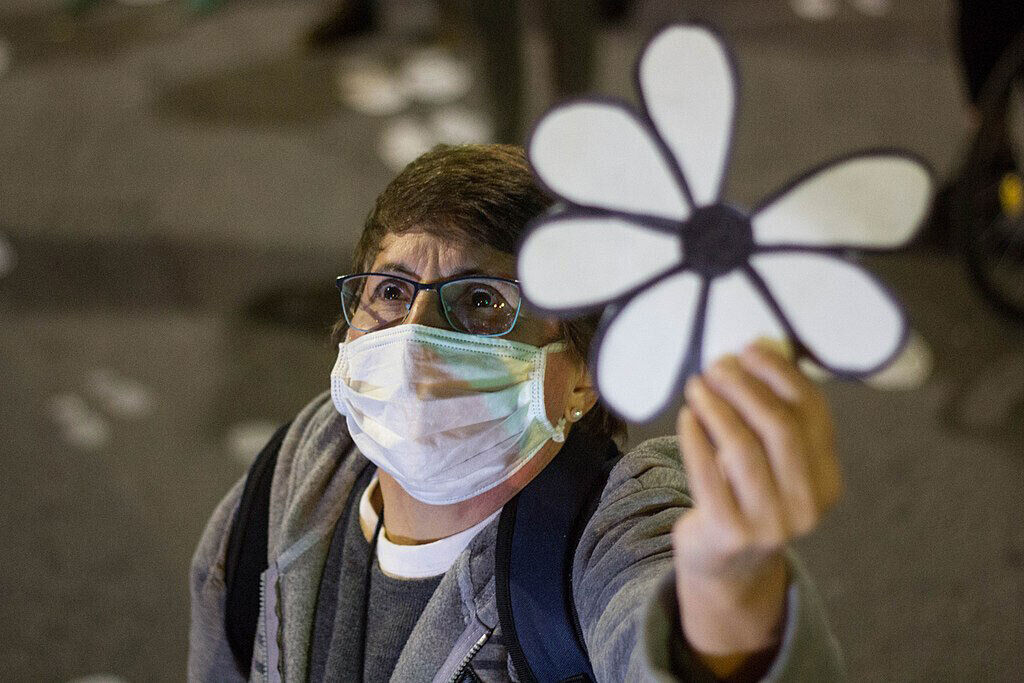 Señora de tapabocas levantando una margarita a la cual le falta un pétalo y representa a los desaparecidos en época de dictadura